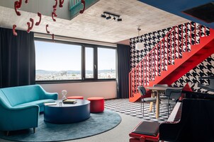 Uma sala de estar moderna com um sofá azul, pufes vermelhos, um piano e uma escada com padrão xadrez preto e branco estilo pied-de-poule.