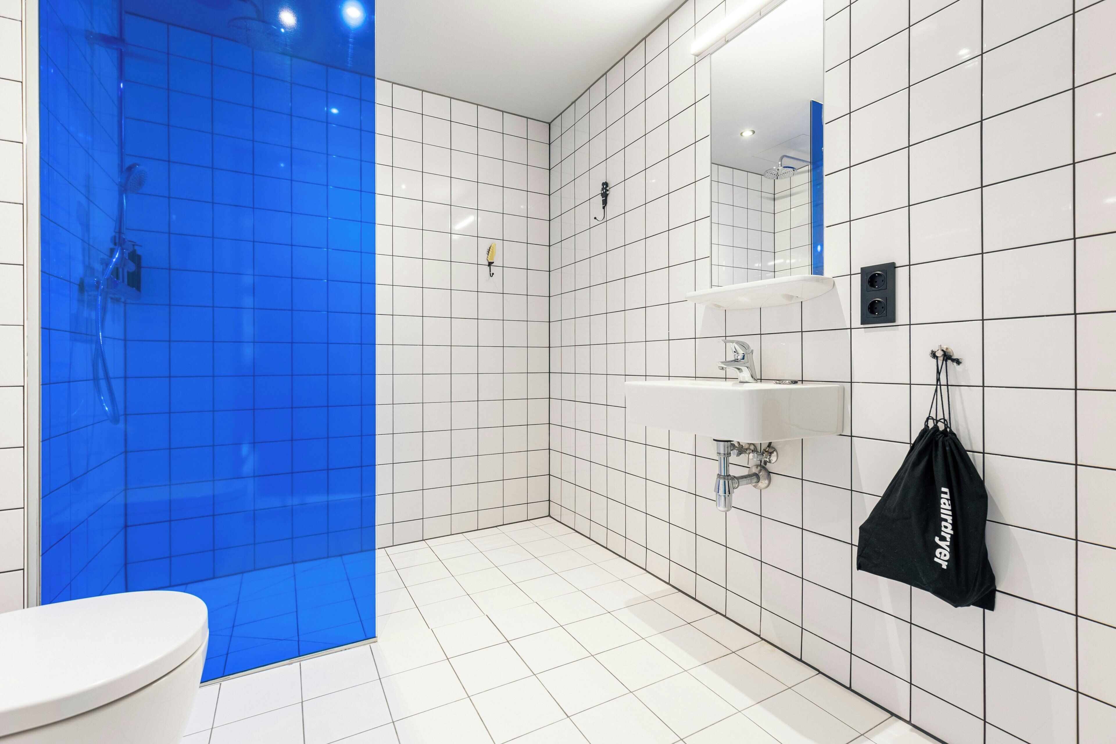 Un baño moderno con azulejos blancos y azules, un inodoro, un lavabo y una ducha.
