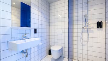 A modern bathroom with white tiles, a white sink, a toilet, and a shower.