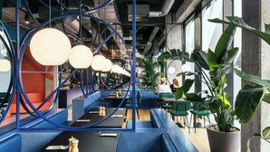 Restaurante moderno com assentos azuis, luminárias pendentes grandes e plantas em vasos.