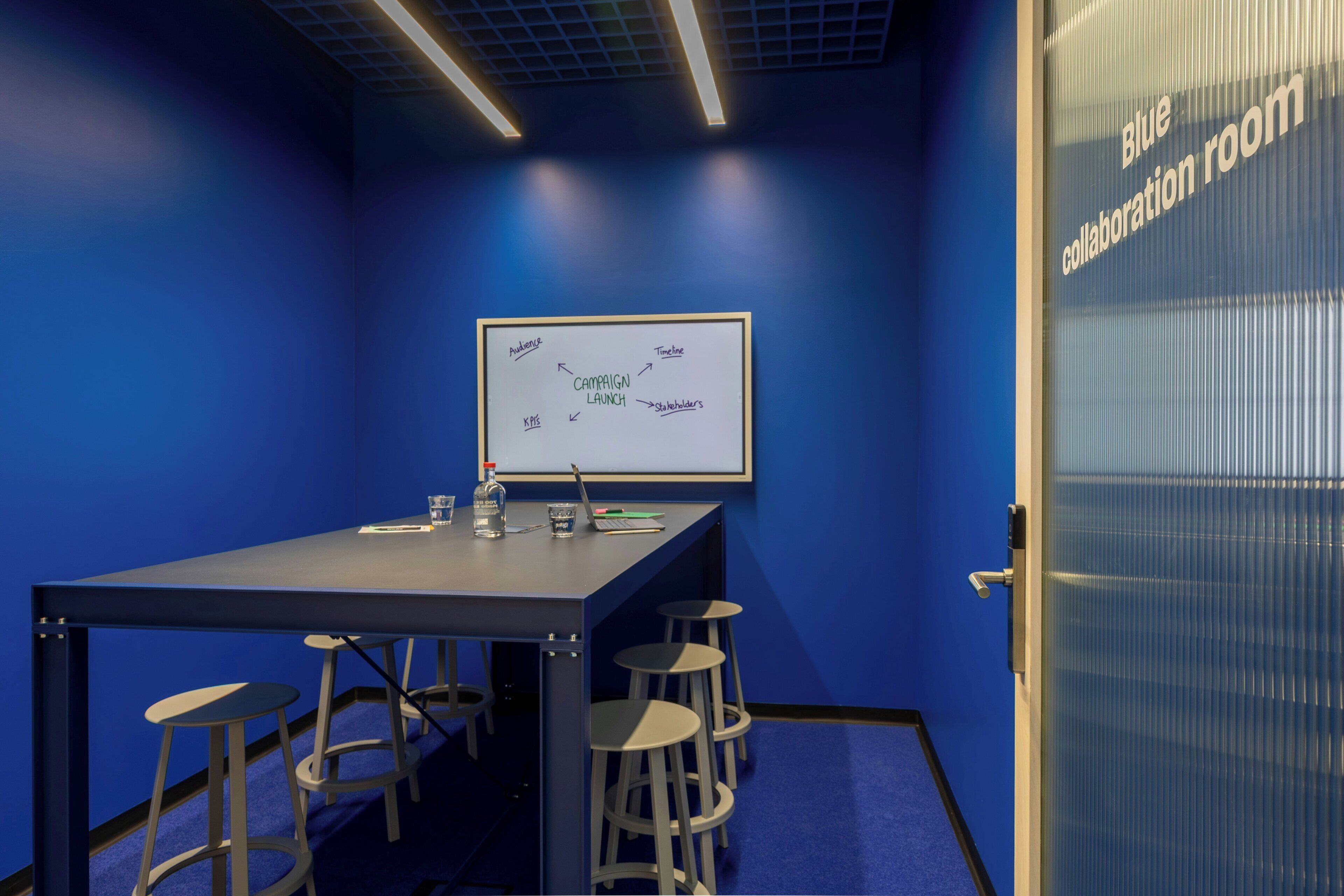 Una sala riunioni blu con lavagna, tavolo e sgabelli.