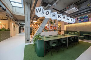 Um espaço de trabalho moderno com mesa de vidro, carpete verde e um letreiro com a palavra 'WORKHARD'.