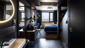 Quarto de hotel moderno com um espelho grande, uma escrivaninha, uma cama e vista para a cidade.