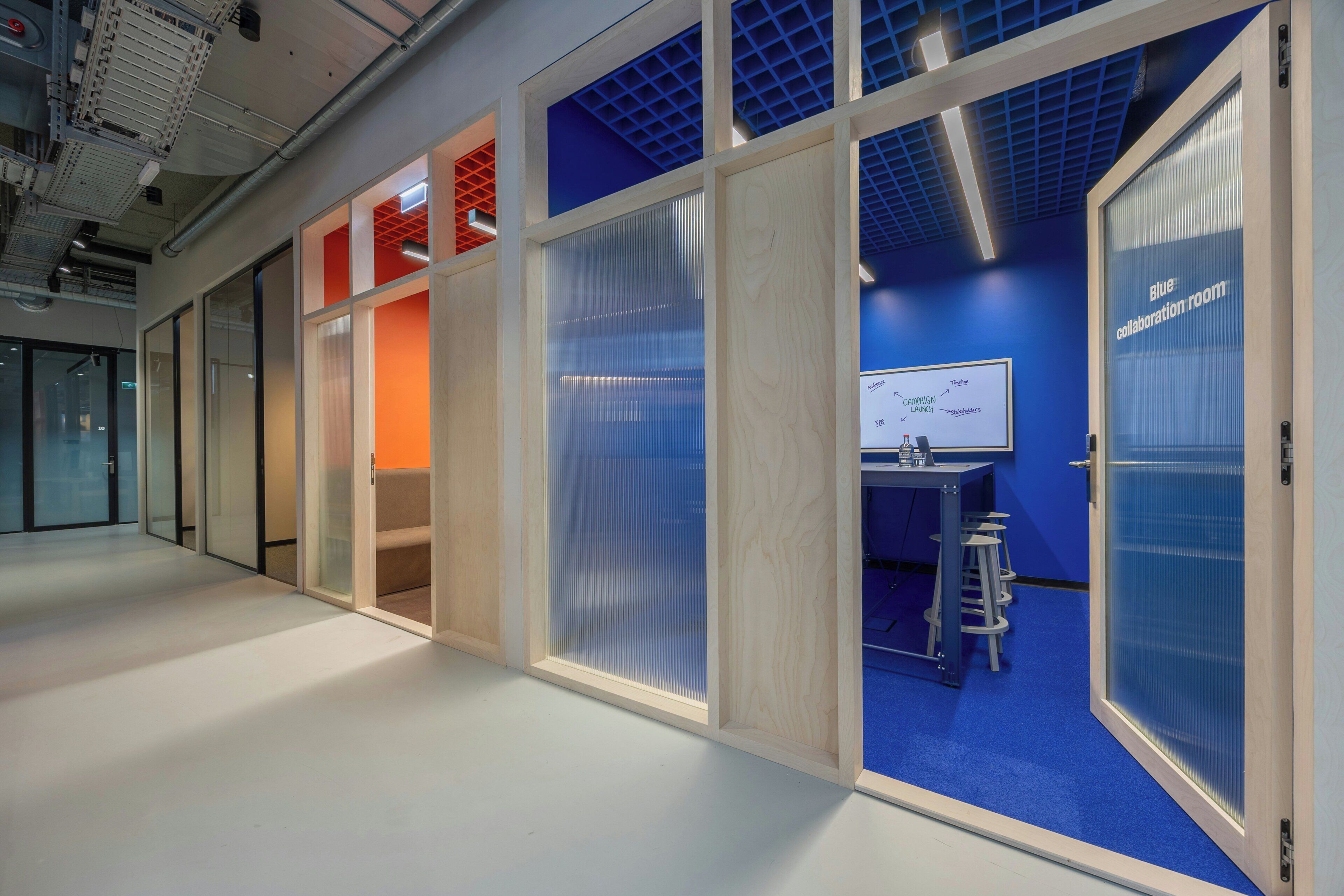 An office space with a collaboration room, a whiteboard, and a blue carpet.