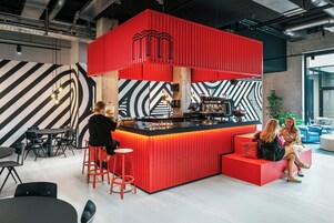 Uma área de bar moderna com parede em vermelho, parede estampada em preto e branco, e um espaço com banquetas.