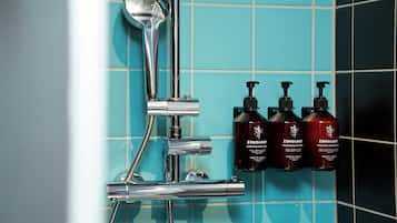 Un cabezal de ducha cromado, una ducha de mano y tres botellas de productos Zenology sobre una pared de azulejos.