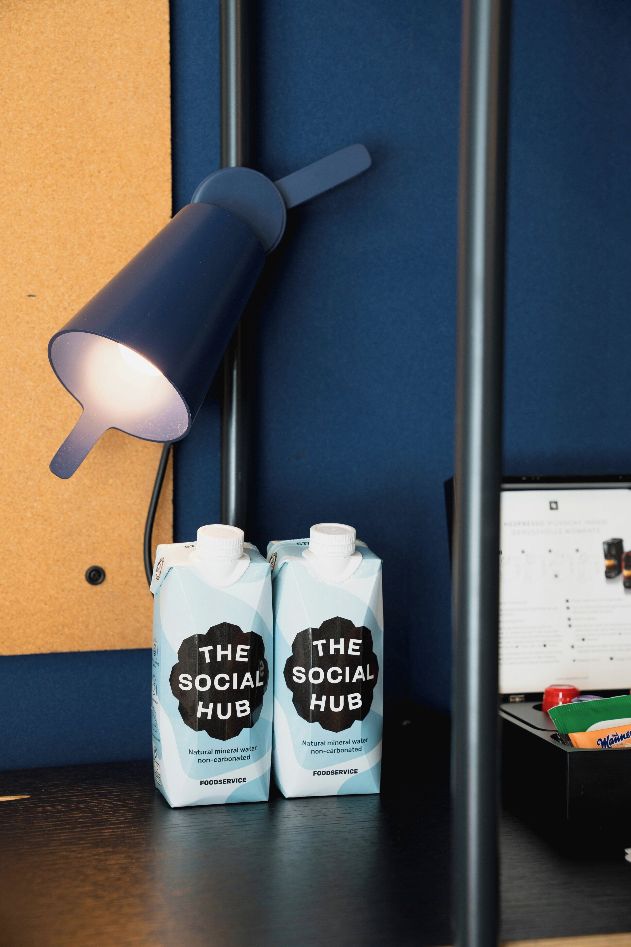 Two cartons of 'The Social Hub' non-carbonated mineral water on a table with a desk lamp and a calendar.