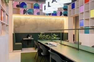 Um espaço de escritório moderno com uma mesa comprida, cadeiras, uma parede verde como destaque e uma estante com formas geométricas coloridas.