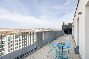 A balcony with a table and chairs, overlooking a cityscape with buildings and a river. - The Social Hub Vienna (Vienna)