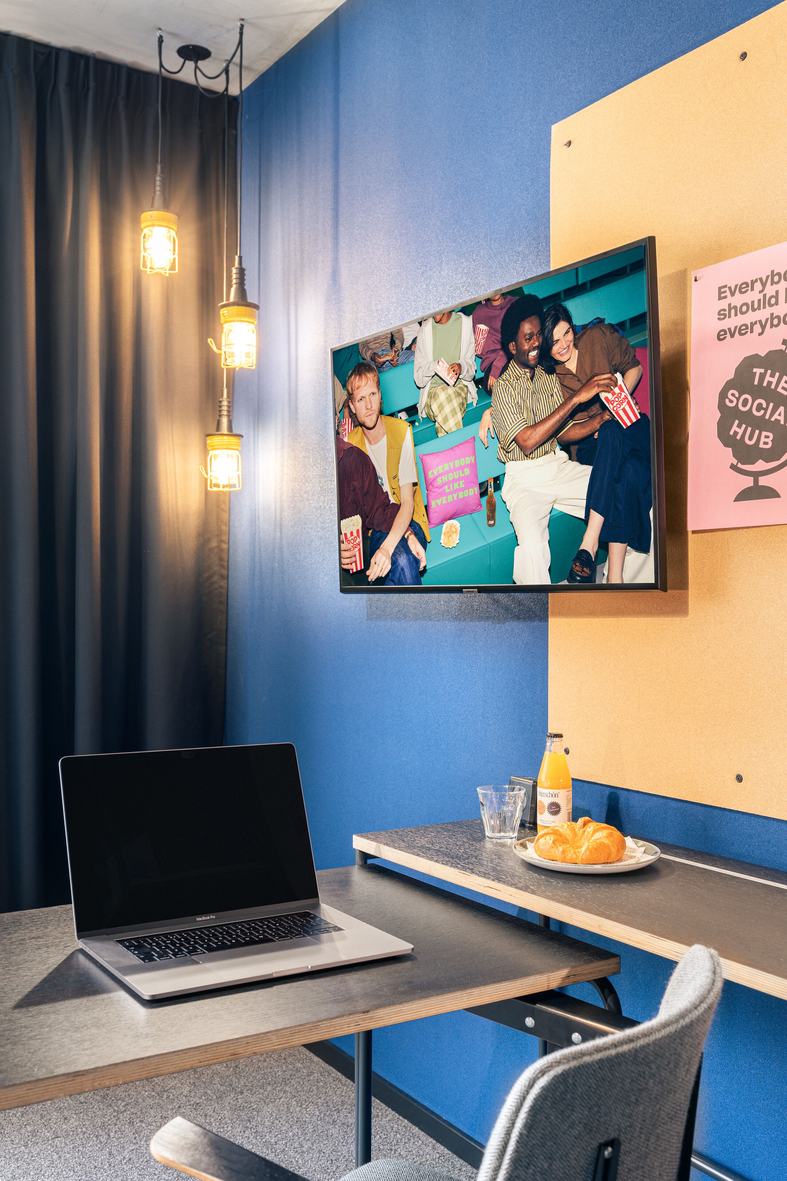Una habitación moderna con una computadora portátil sobre una mesa, un televisor en la pared y un cartel.