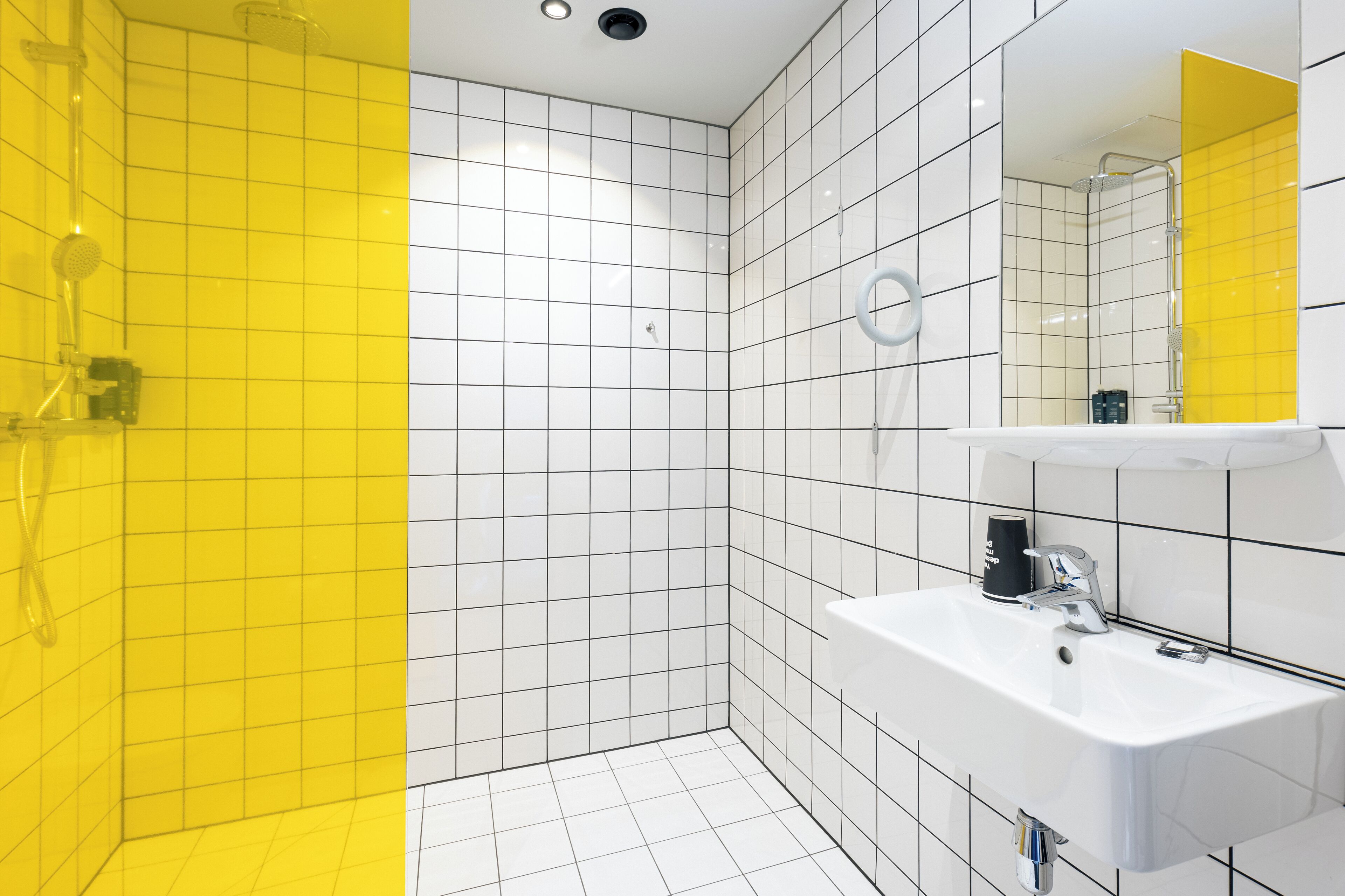 Un baño moderno con baldosas blancas y amarillas, un lavamanos blanco y una zona de ducha.