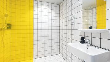 Uma casa de banho moderna com azulejos brancos e amarelos, uma sanita branca e uma área de chuveiro.