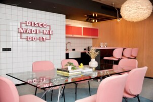 Uma sala de jantar moderna com mesa de vidro, cadeiras cor-de-rosa e um letreiro de neon na parede.