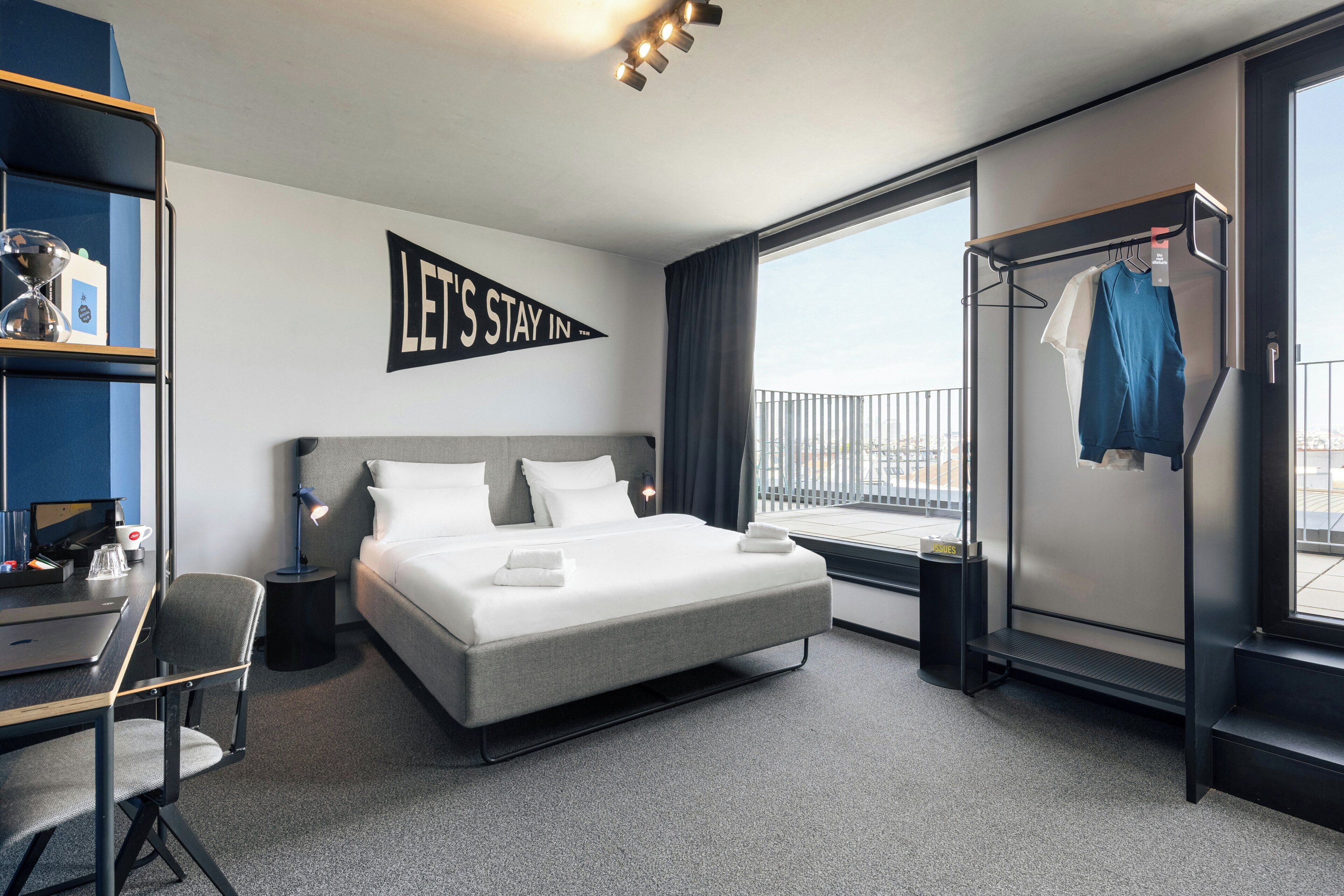 Ett modernt hotellrum med en säng, ett skrivbord, en stol och utsikt över staden.