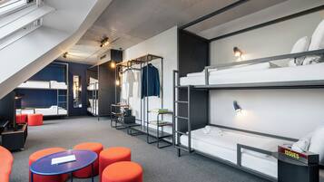 Une chambre d’hôtel moderne équipée de lits superposés, d’un bureau et d’un coin salon avec des poufs.