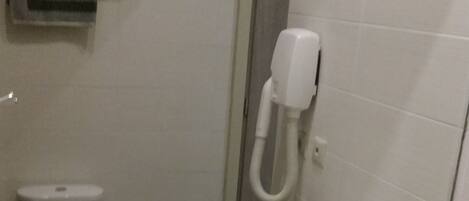 A bathroom with a white sink, a mirror, and a toilet. There are two rolls of toilet paper and a soap dispenser on the wall.
