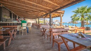 Una terraza de madera con mesas y sillas, una zona de bar y vistas al mar.