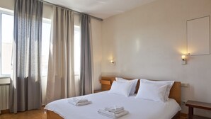 A hotel room with a large bed, two bedside tables, a radiator, and a window with curtains. - Impressive Apartment with Amazing Views in Athens City Centre! MK1 (Athens)