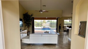 A spacious living area with a white sofa, a ceiling fan, and a view of a swimming pool. - Southern Sun Beach Hotel - Cape Coral (Cape Coral)