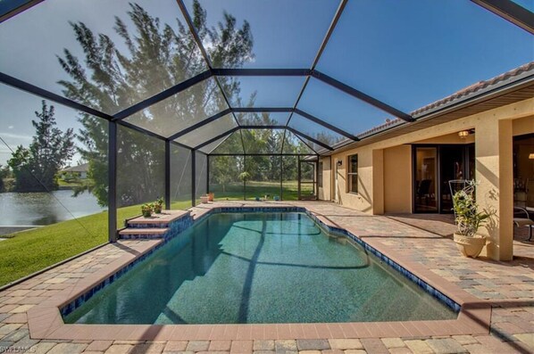 Relax in a serene pool area surrounded by a lawn and trees, adjacent to a building with large glass doors.
