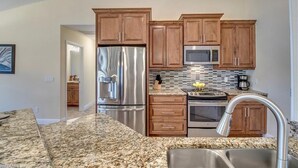 A modern kitchen with granite countertops, stainless steel appliances, wooden cabinets, and a ceiling fan. - Southern Sun Beach Hotel - Cape Coral (Cape Coral)