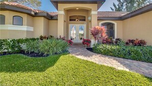 A residential building with a tiled roof, a central entrance with a door, and a landscaped garden with various plants and a paved walkway. - Southern Sun Beach Hotel - Cape Coral (Cape Coral)