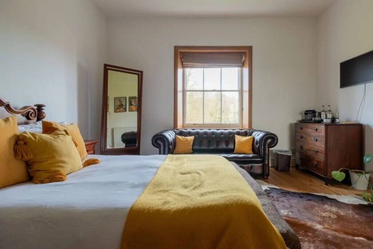 A bedroom with a bed, a sofa, a dresser, and a window.