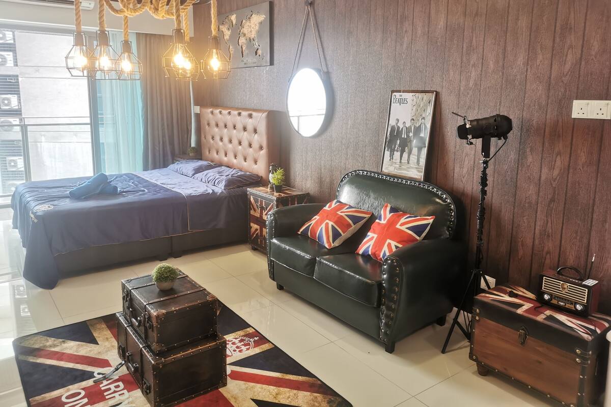 A modern bedroom with a bed, a leather sofa with Union Jack pillows, a vintage radio, and a world map on the wall.