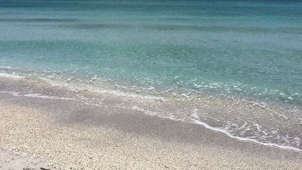 Une plage à l’eau turquoise et limpide, bordée d’un rivage sablonneux.