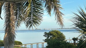 Une vue sur la côte, avec un palmier, une zone sablonneuse et un pont au loin.
