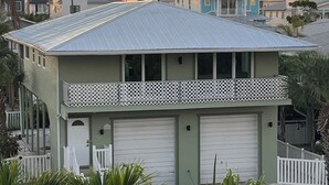 Une maison à deux étages, avec un toit en métal, un balcon doté d’une balustrade en treillis et un garage.