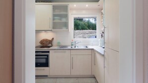 Une cuisine moderne avec des armoires blanches, un four encastré et une fenêtre donnant sur les arbres.