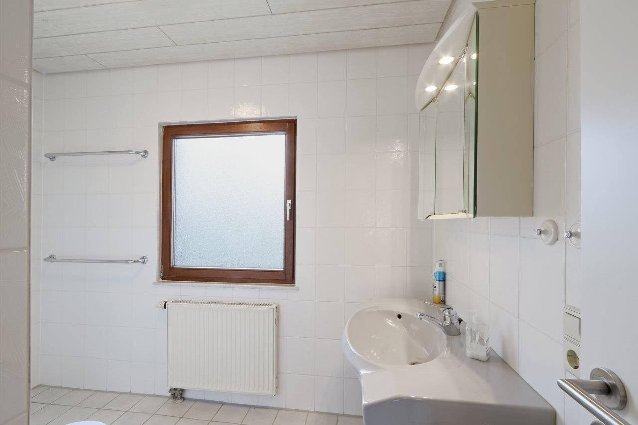 Ein modernes Badezimmer mit Fenster, Heizkörper, Waschbecken und Spiegel.