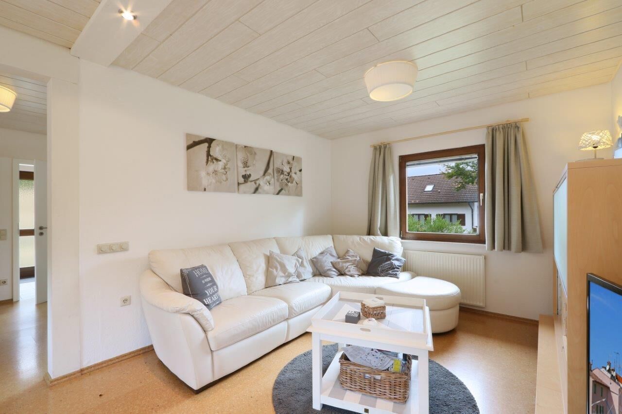 A modern living room with a white sofa, a round coffee table, and a large window with curtains.