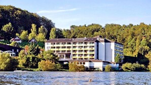 Un hôtel à plusieurs étages, doté de balcons, situé près d’une étendue d’eau, avec des arbres en arrière-plan.