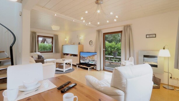 Un salon moderne doté d’un plafond en bois, d’un téléviseur à écran plat, d’un coin repas avec une table et des chaises, et d’une cheminée.