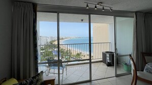Een balkon met uitzicht op het strand en de oceaan, een schuifdeur, een kleine tafel en een stoel.
