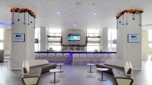 Een moderne hotel lobby met een receptiebalie, een zithoek en een televisiescherm.