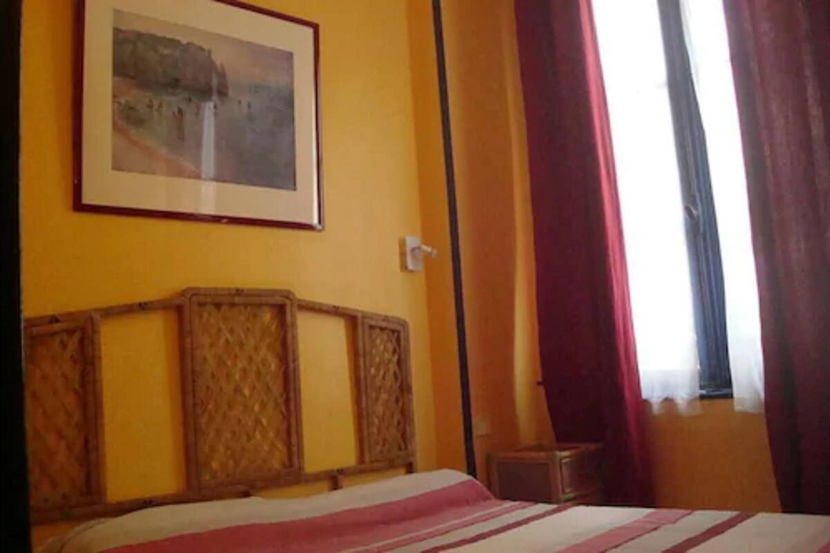 Una habitación de hotel con una cama, un cuadro en la pared y una ventana con cortinas.