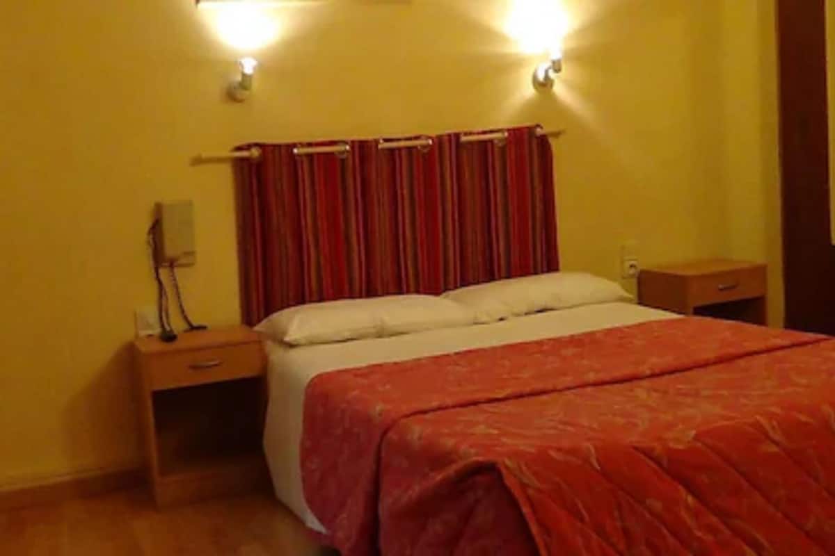Un dormitorio con una cama, dos mesitas de noche y una lámpara de pared.