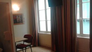 A room with a bed, a desk, and a chair. There is a window with curtains. - Hôtel du Palais (Rouen)