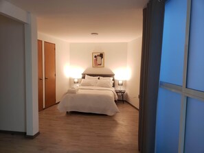 A hotel room with a bed, bedside lamps, a nightstand, and a door. - Darwin8 (Mexico City)