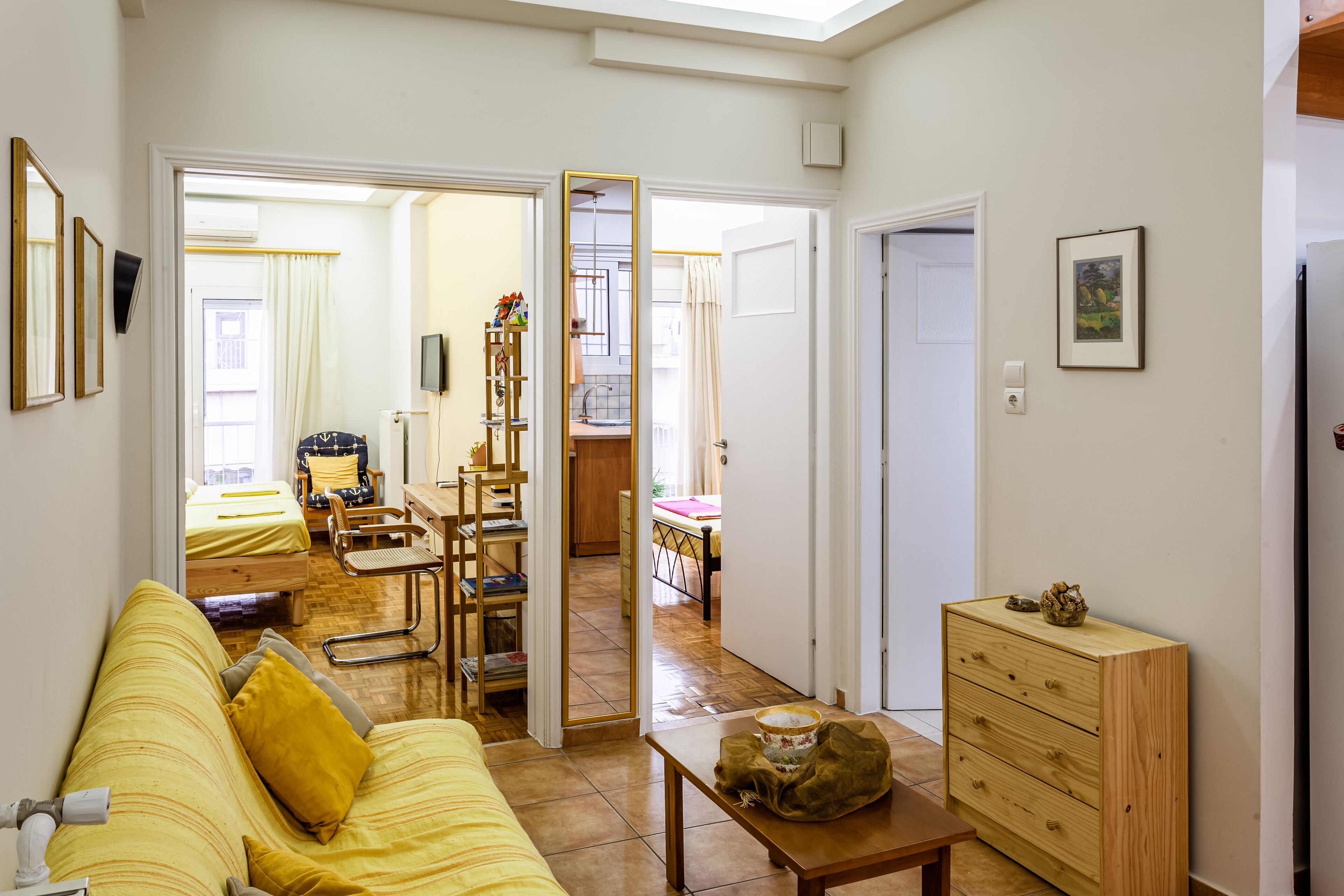 A room with a yellow sofa, a wooden dresser, and a dining area with a table and chairs.