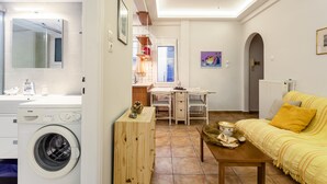 A compact living space with a washing machine, a dining area, a sofa, and a ceiling fan. - Zografou Hidden Gem - Athens Charming Home (Zografos)