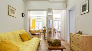 A bright living room with a yellow sofa, a wooden table, and a wooden dresser. There is a large mirror on the wall, and a door leading to another room. - Zografou Hidden Gem - Athens Charming Home (Zografos)