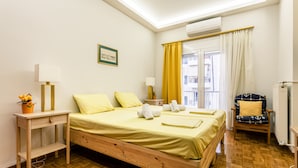 A hotel room with a wooden bed, a bedside table with a lamp, a chair with a cushion, and a window with curtains. - Zografou Hidden Gem - Athens Charming Home (Zografos)