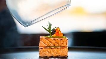 A glass of water being poured onto a salmon tartare dish with a garnish.