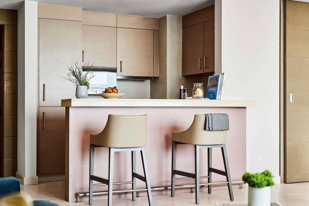 A modern kitchen with a central island, two bar stools, and a small potted plant.