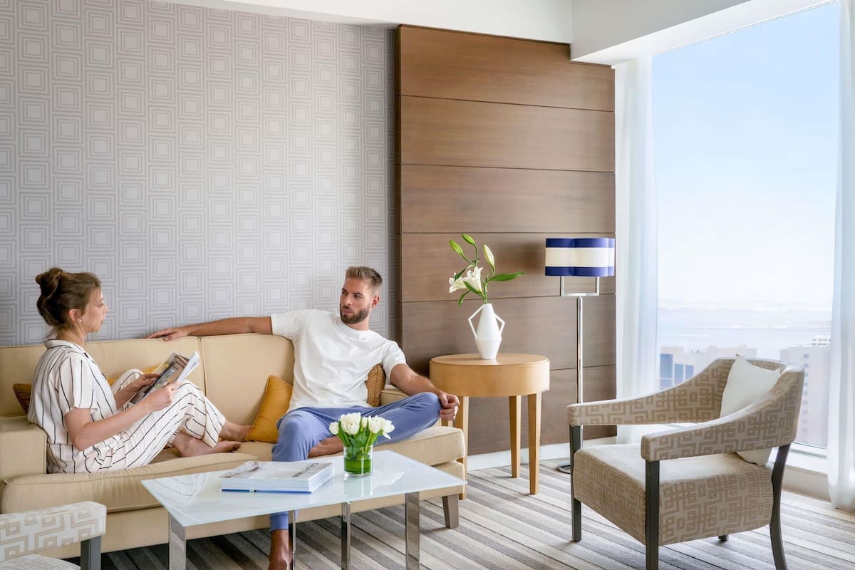 A modern hotel room with a sofa, a coffee table, a side table with a vase, and a chair.