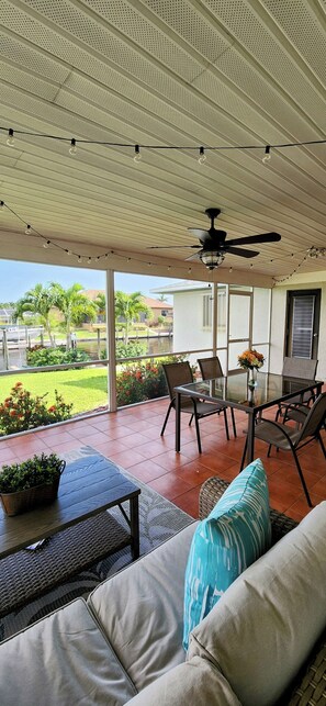 Eine Terrasse im Freien mit Deckenventilator, Glastisch und Stühlen.